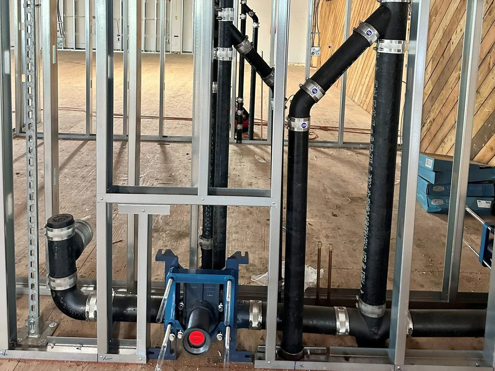 Cast iron waste and vent with no-hub couplings in open steel framing, a toilet carrier at the floor