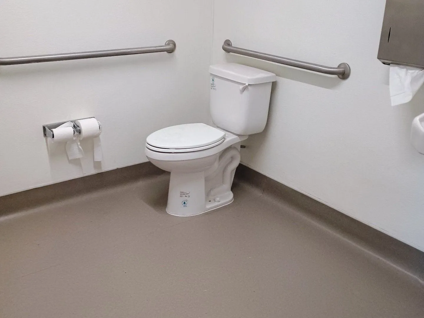 Accessible restroom with a tank toilet and grab bars on a taupe floor