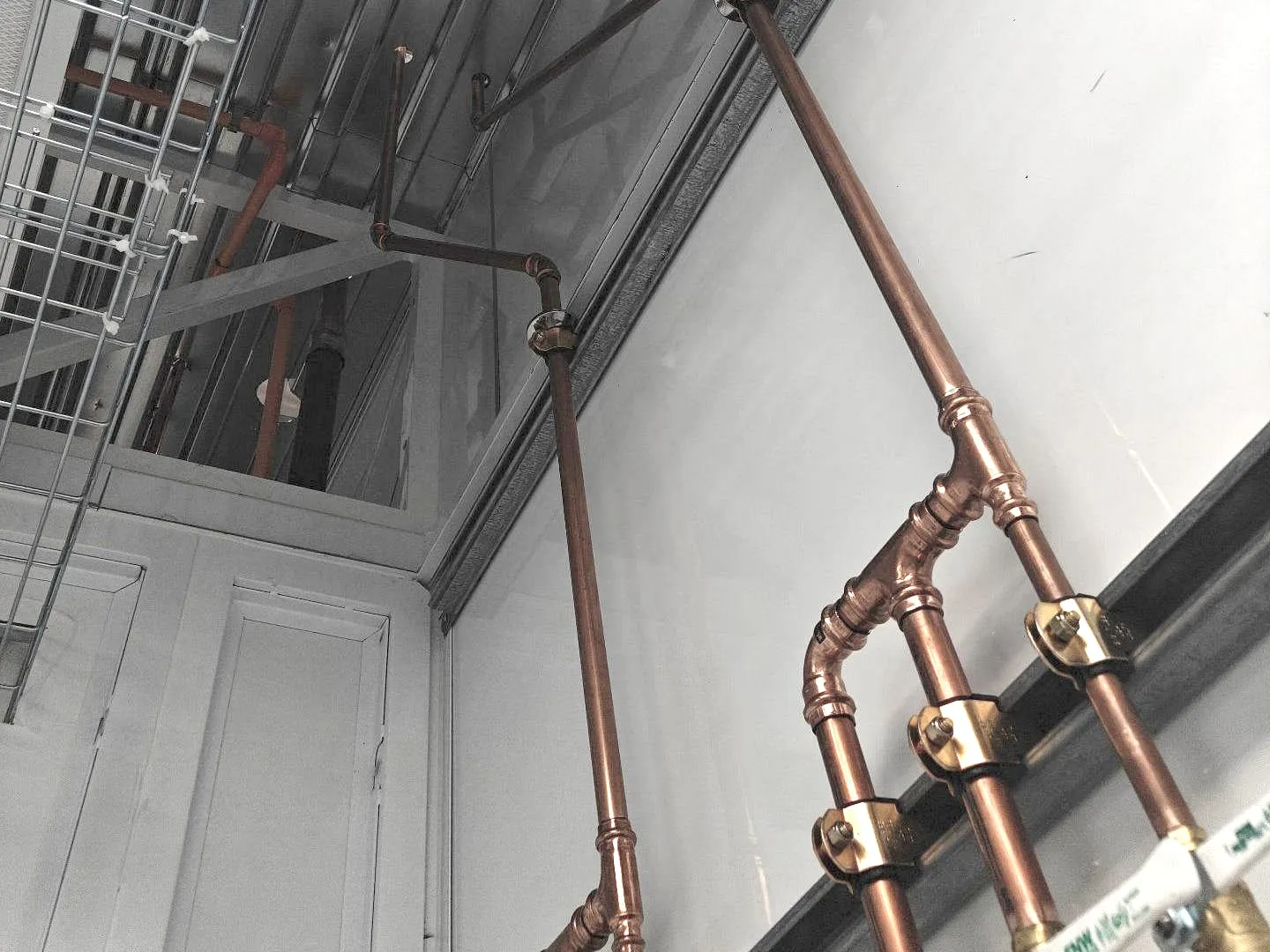 Copper water lines with press fittings climbing a white wall toward the ceiling