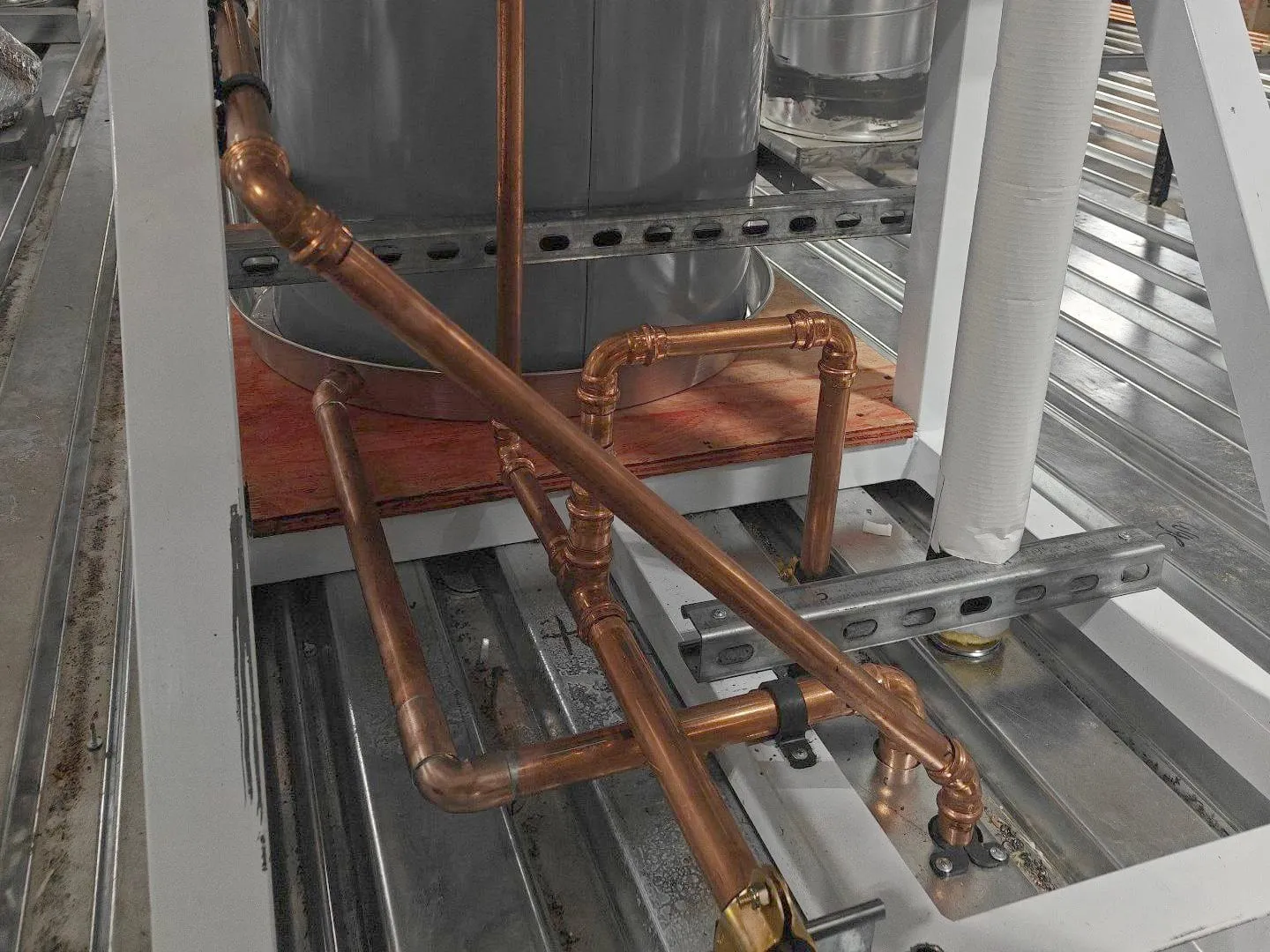Copper piping on strut at the base of a water heater, beside its drain pan