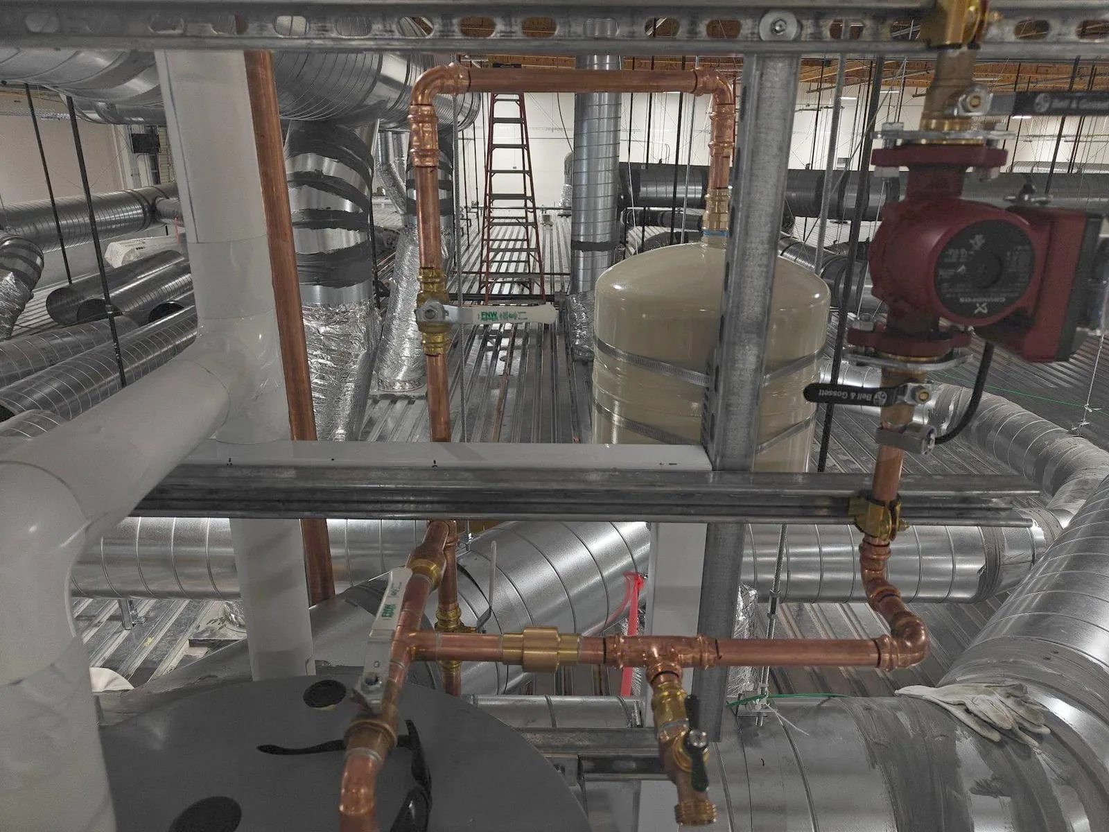 Copper piping with ball valves and an expansion tank on strut above a water heater, among ducts
