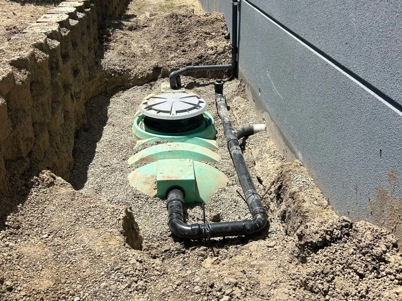 Green holding tank set in gravel in an excavation outside a building wall