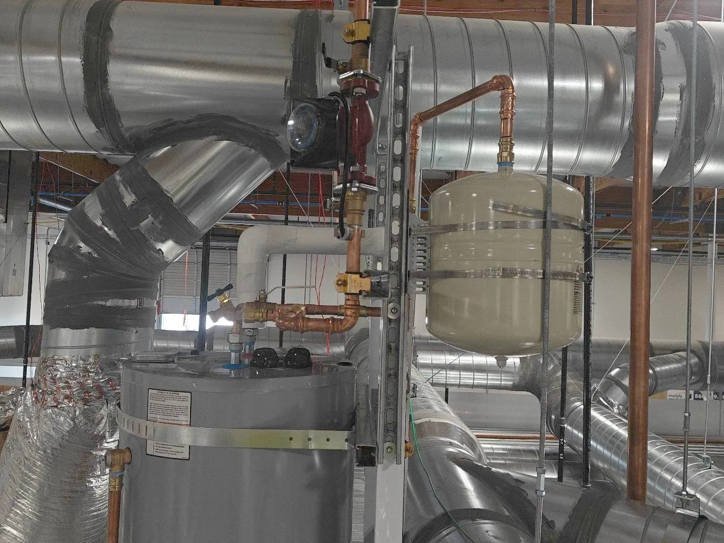 Electric water heater with its expansion tank and copper piping on a mezzanine among ducts