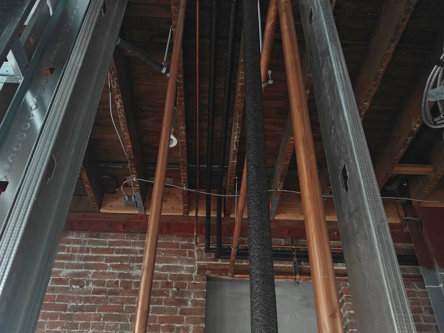 Copper risers running up through steel framing past an original brick wall