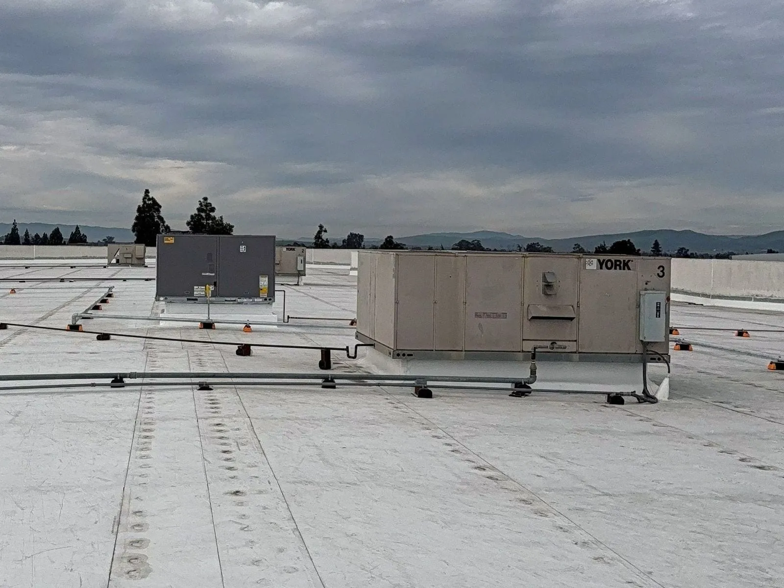 Rooftop HVAC units on a white roof with gas piping on supports running to them