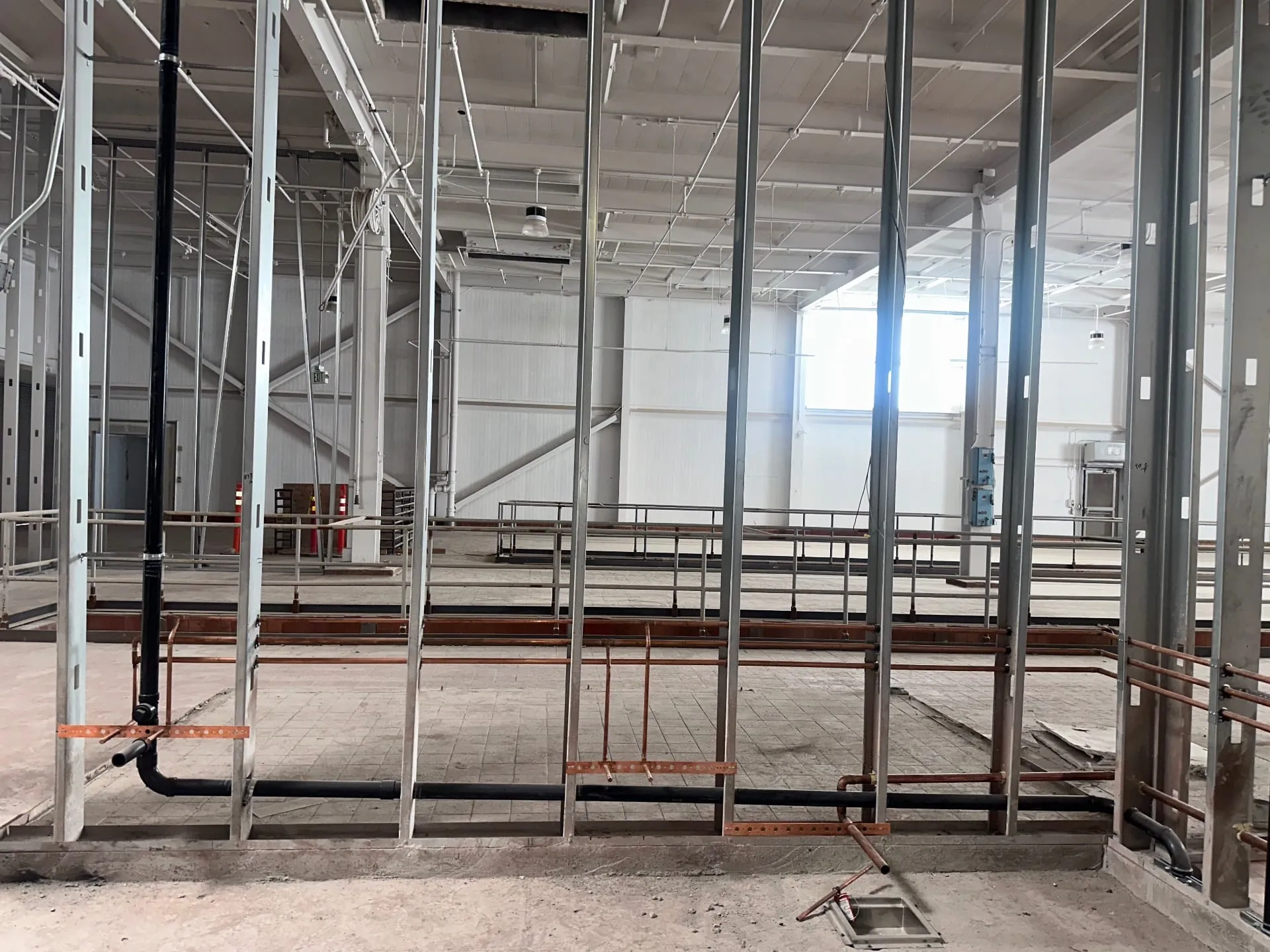 Copper water and black waste piping roughed in through open steel framing in a bright warehouse