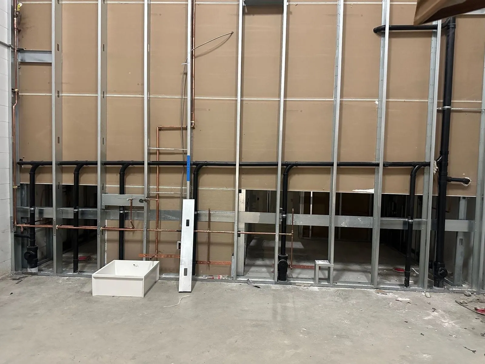 A long framed wall with black waste and copper water roughed in to a row of fixtures