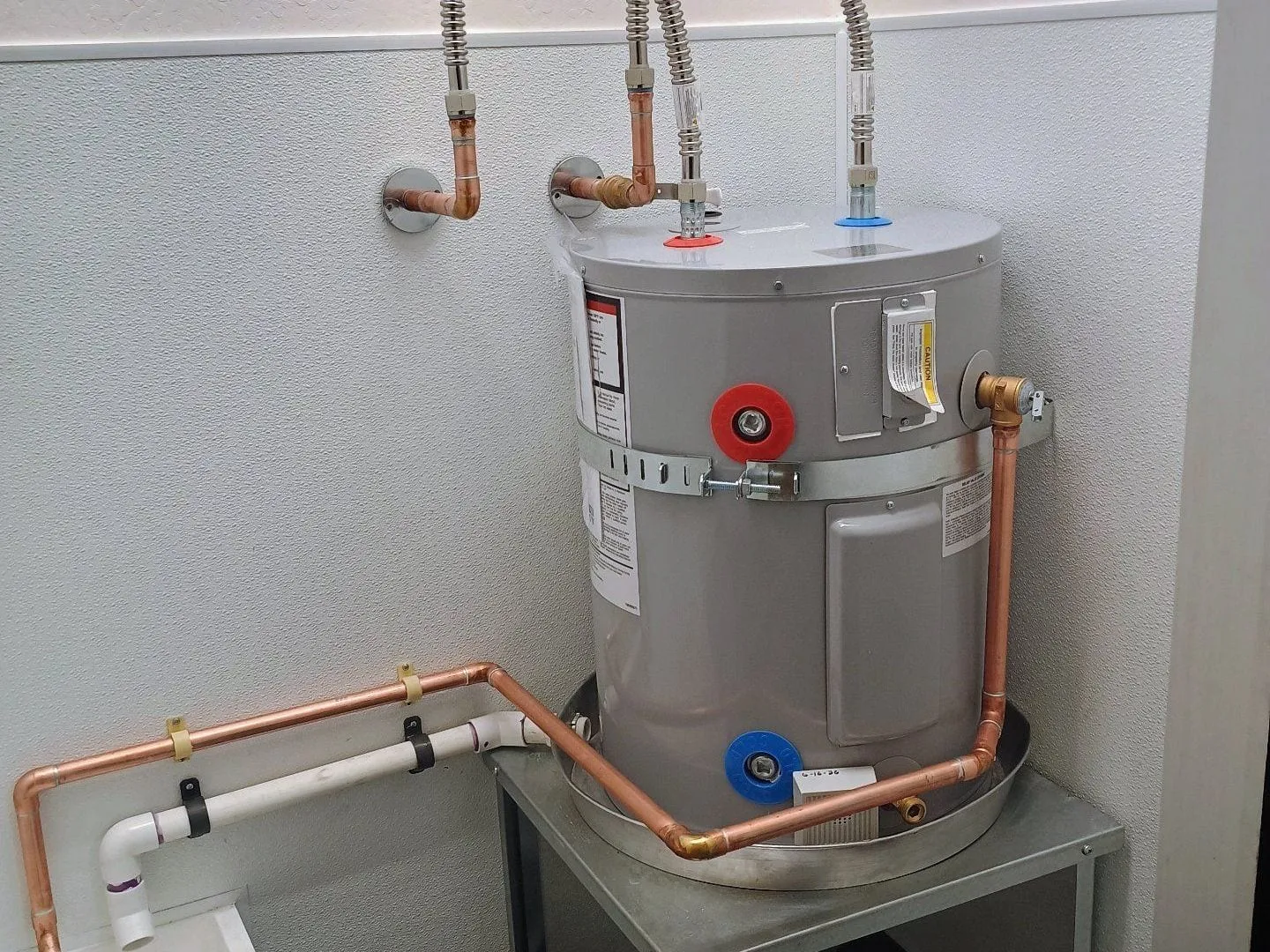 Electric water heater on a steel stand in a janitor's closet, piped in copper with flexible connectors